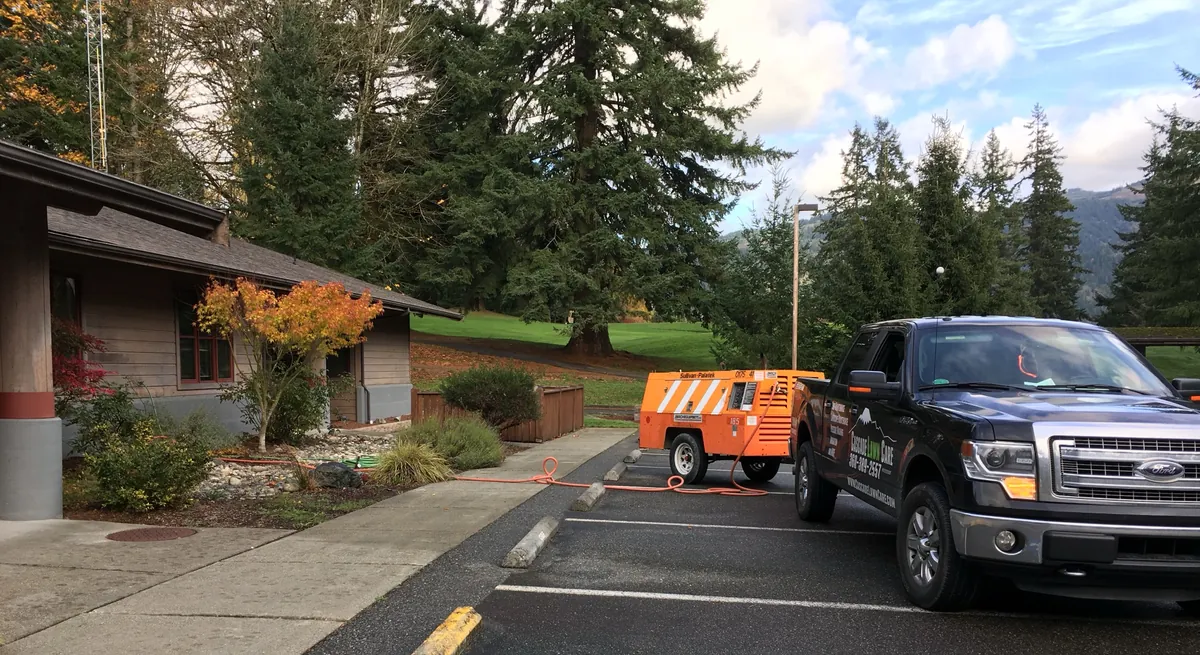 Our orange tow-behind air compressor parked behind a Cascade Lawn Care truck, with its hose running into a planting bed