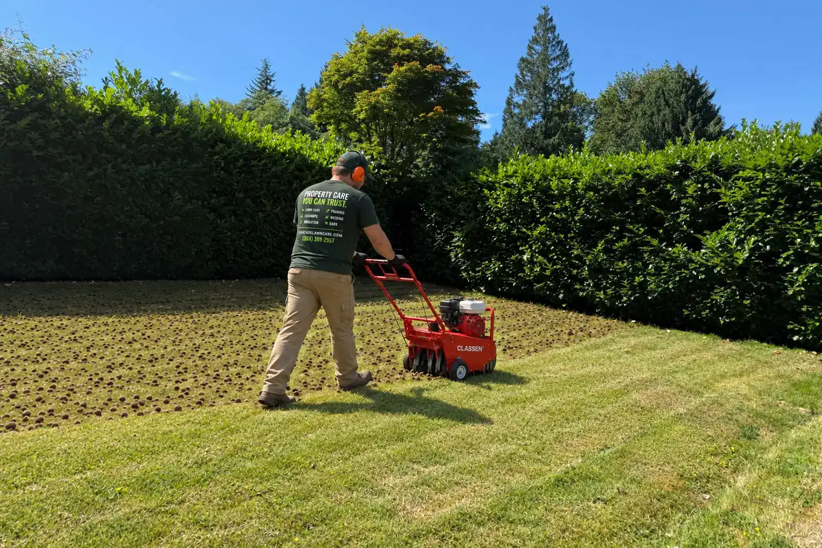 A Cascade Lawn Care crew member core-aerating a lawn, with the finished lawn behind him covered in plugs